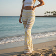 Woman wearing patterned pants and a white top on a beach