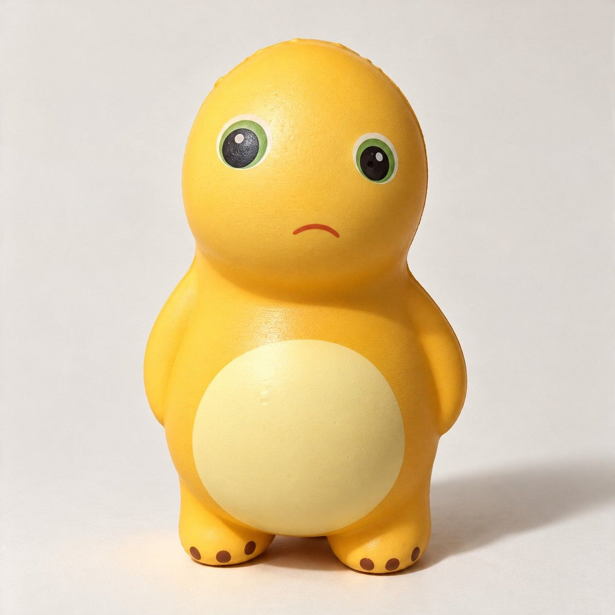 Yellow dinosaur squishy with green eyes, a little frown and a cream belly, front view