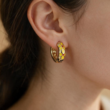Yellow flower enamel open hoop earring with red and black accents worn on the ear
