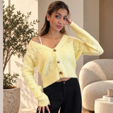 Pale yellow pointelle knit cardigan with brown buttons, hand at hair