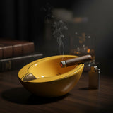 Side view of a deep yellow ash bowl holding a lit cigar next to a lighter and books