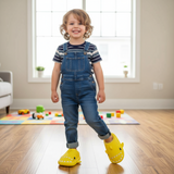 Toddler in denim dungarees stepping forward in bright yellow shark slippers