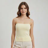 Woman wearing a light yellow spaghetti strap top against a plain background