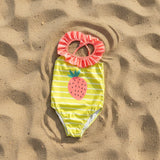 Yellow strawberry print swimsuit flat lay on sand