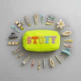Yellow pouch with 'STUFF' text surrounded by colorful hair clips on a grey background