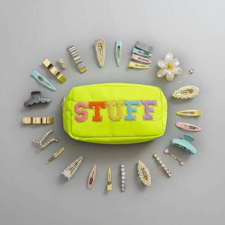 Yellow pouch with 'STUFF' text surrounded by colorful hair clips on a grey background