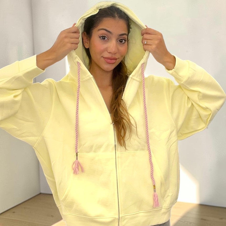 Pale yellow hoodie worn with the hood up and the long tassel cords hanging loose