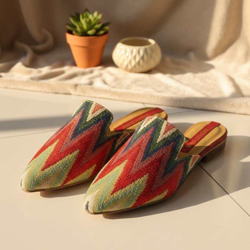 Colorful zigzag patterned handmade slippers on a light surface with a plant in the background