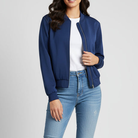 Woman wearing a blue bomber jacket and light blue jeans on a plain background