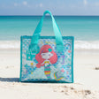 Mermaid-themed tote bag on a sandy beach with a mountain in the background