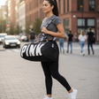 Woman walking on a city street holding a black 'PINK' duffel bag.