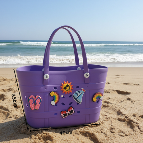 Purple beach bag with decorative stickers on a sandy beach with ocean waves in the background