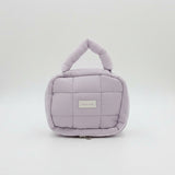 Purple quilted handbag with a visible brand label on a white surface, with pink and peach bags in the background.