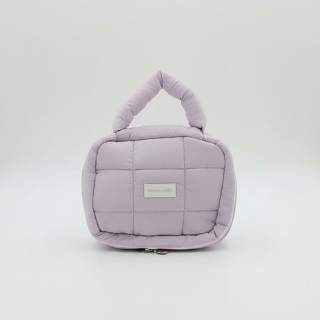 Purple quilted handbag with a visible brand label on a white surface, with pink and peach bags in the background.