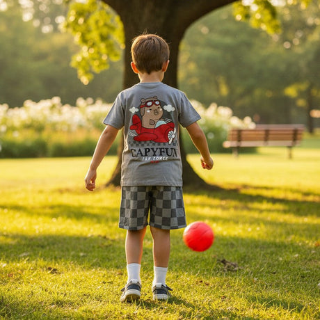 Child playing with a red ball in a park with a large tree in the background