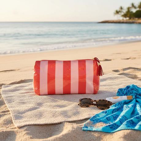 Red and white striped bag, sunglasses, and towel on a sandy beach with ocean view
