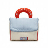 Baby bag with quilted top and red handle with 'Milo Bliss' branding, displayed in a store setting.
