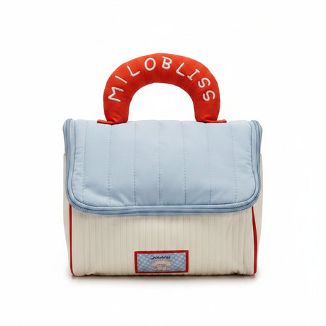 Baby bag with quilted top and red handle with 'Milo Bliss' branding, displayed in a store setting.