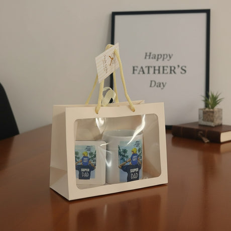 Two mugs in a gift bag with 'Super Dad' design on a wooden surface, framed by 'Happy Father's Day' text.