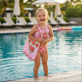 Child in a pink swimsuit with watermelon design standing by a pool.